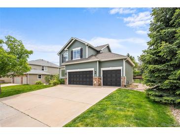 Charming two-story home featuring a three-car garage, green lawn, and lush landscaping at 10802 W Indore Dr, Littleton, CO 80127
