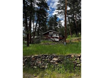Charming cabin-style home nestled among tall trees with a stone retaining wall in the foreground at 27447 Upper Cold Spg Gulch Rd, Golden, CO 80401