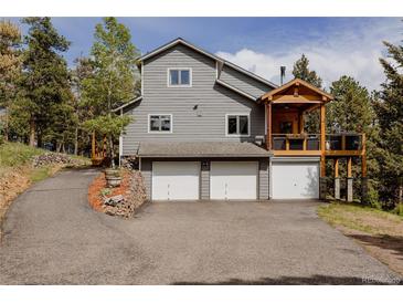 View of a gray two-story home with three garage doors and a wooden porch at 8626 Junco Trl, Evergreen, CO 80439