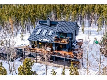 Stunning mountain home with metal roof and multiple decks, surrounded by snow-covered landscape and evergreen trees at 10756 Timothys Dr, Conifer, CO 80433