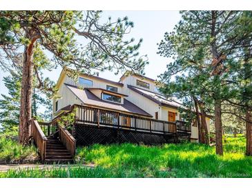 Charming home featuring a large deck and stairs surrounded by lush greenery and mature trees at 24999 Grandview Ave, Golden, CO 80401