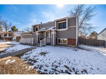 Charming gray two-story home featuring a covered front porch and snow-covered yard at 15716 E Temple Pl, Aurora, CO 80015