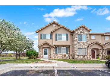 Charming townhome featuring a stone facade, well-maintained landscaping, and a lovely flowering tree at 12798 Ivy St, Thornton, CO 80602