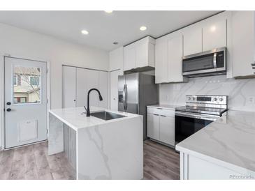 Modern kitchen featuring a waterfall island, stainless steel appliances, and white cabinets for a clean aesthetic at 12798 Ivy St, Thornton, CO 80602