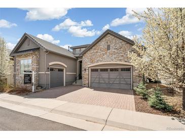 Stunning two-story home with a stone and stucco exterior, a three-car garage and a brick driveway at 5943 S Olive Cir, Centennial, CO 80111