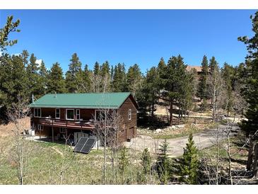 Charming cabin with a green roof, wrap-around balcony and beautiful forest surroundings on a sunny day at 72 Rudi W Ln, Golden, CO 80403