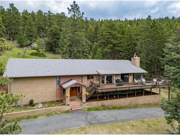 Charming brick home boasts a spacious deck with scenic views of surrounding lush green trees at 7815 Armadillo Trl, Evergreen, CO 80439