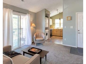 Cozy living room with a sliding glass door to the balcony, and a stacked washer and dryer at 9640 W Chatfield Ave # A, Littleton, CO 80128