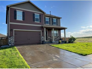 Two-story home with a well-manicured lawn, brown siding, stone accents, and a two-car garage at 975 Alta St, Lochbuie, CO 80603