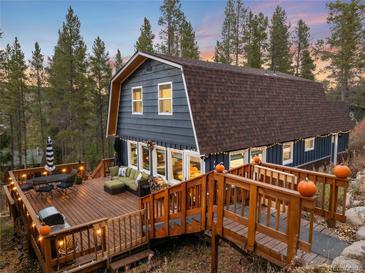 Charming barn style house with a wooden deck featuring outdoor seating, grill, and string lights in a wooded setting at 384 Blue Ridge Rd, Breckenridge, CO 80424