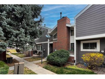 Townhome featuring gray siding, a brick chimney, and well maintained landscaping at 6625 W 84Th Cir # 48, Arvada, CO 80003