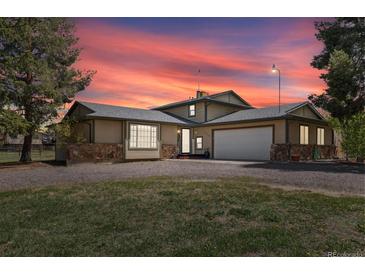 Inviting tan home with stone accents, two-car garage, mature trees, and gravel driveway at dusk at 1866 Mountain View St, Erie, CO 80516