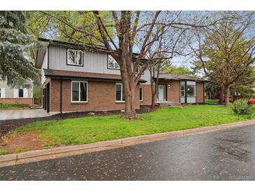 Charming two-story home featuring a brick facade, gray siding, lush lawn, and mature trees at 11351 Quivas Way, Denver, CO 80234