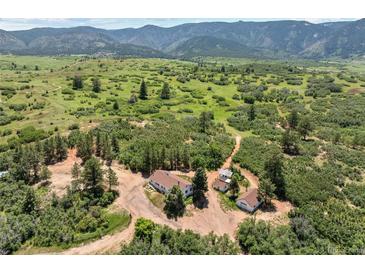 Expansive aerial view showcases a secluded home nestled among lush greenery and rolling hills against a mountain backdrop at 8821 S Perry Park Rd, Larkspur, CO 80118