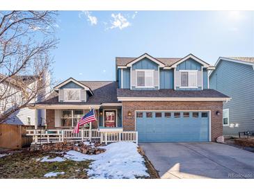 Charming two-story home features a brick facade, blue siding, an attached garage, and a welcoming front porch with an American flag at 9839 Foxhill Cir, Highlands Ranch, CO 80129