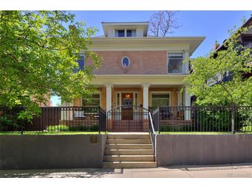 Charming two-story brick home featuring a covered porch, iron fence, and manicured landscaping at 747 N Downing St, Denver, CO 80218