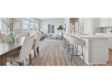 Open-concept living space with bright windows, sleek flooring, and modern kitchen island with bar seating at 21091 E 63Rd Dr, Aurora, CO 80019