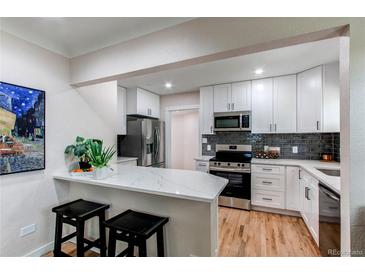 Bright kitchen boasts white cabinets, stainless steel appliances, quartz counters, and eat-in bar at 1969 Uinta St, Denver, CO 80220