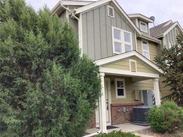 Exterior view of a two-story townhome featuring neutral siding, brick accents, and lush evergreens near the entry at 11947 Riverstone Cir # 7F, Henderson, CO 80640