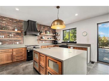 Modern kitchen featuring a brick accent wall, stainless steel appliances, floating shelves, and a large center island at 10731 E 151St Pl, Brighton, CO 80602