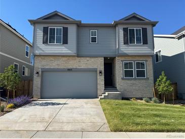 Two-story home featuring stone and gray siding, a two-car garage, well-manicured lawn, and tasteful landscaping at 16651 W 93Rd Ave, Arvada, CO 80007