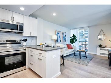 Bright living room with modern kitchen, stainless appliances, balcony, and light wood flooring at 830 N Sherman St # 205, Denver, CO 80203