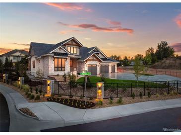Beautiful stone home with a manicured lawn, metal fence, and an attached three car garage at 6541 S Harlan Ct, Littleton, CO 80123