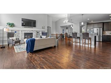 Open-concept living room features a fireplace, hardwood floors, and adjacent kitchen with bar seating at 9060 Ferncrest St, Firestone, CO 80504