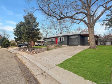 Charming gray home featuring a red front door, attached garage, mature trees, and a well-maintained front lawn at 9639 W 63Rd Pl, Arvada, CO 80004
