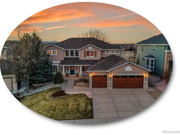 Beautiful two-story home featuring a well-manicured lawn, mature trees, and a two-car garage under a colorful sky at 9845 Glenstone Trl, Highlands Ranch, CO 80130