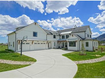 Beautiful white farmhouse exterior with a basketball hoop and long curved driveway at 609 Pioneer Camp Vw, Palmer Lake, CO 80133