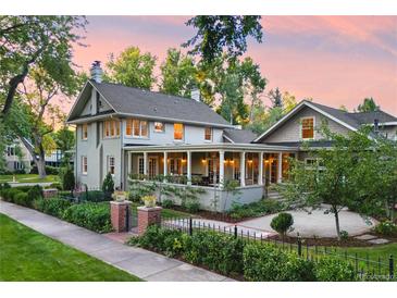 Stunning two-story home with a brick and black metal fence, a beautiful lawn, and a large, inviting wrap-around porch at 3109 E Warren Ave, Denver, CO 80210