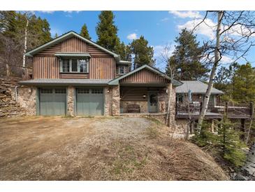 Charming log cabin home with a two-car garage, stone accents and mature trees in the background at 39 Pat Creek Rd, Evergreen, CO 80439