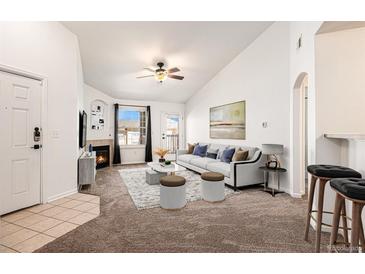 Bright living room featuring vaulted ceilings, a cozy fireplace, neutral carpet, and lots of natural light at 5756 N Genoa Way # 12-305, Aurora, CO 80019