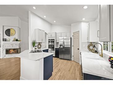 Bright kitchen featuring white cabinets, stainless steel appliances, a large island, and a cozy fireplace nearby at 1896 S Marshall Cir, Lakewood, CO 80232
