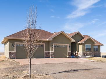 Beautiful single-story home with three-car garage, stone accents and a spacious driveway on a sunny day at 14077 Indianfield Ct, Hudson, CO 80642