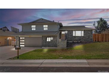Charming home with stone facade, lush lawn, and inviting front entrance at dusk at 6844 W 69Th Pl, Arvada, CO 80003