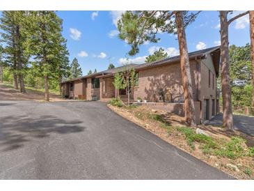 Brick home with an asphalt driveway is surrounded by mature trees and well-maintained landscaping at 7845 Armadillo Trl, Evergreen, CO 80439