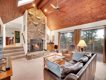 Inviting living room featuring a stone fireplace, wood ceiling, and access to a deck with scenic views at 23485 Bluestem Dr, Golden, CO 80401