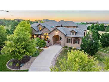 Beautiful home with stone facade, porte-cochère, professional landscaping, and mature trees at sunset at 4839 Bandera Pl, Parker, CO 80134