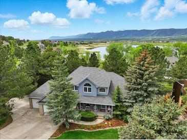 Picturesque aerial view of a two-story home with mature trees, lake, and mountain backdrop at 18590 Lower Lake Rd, Monument, CO 80132