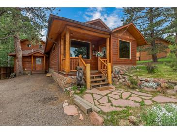 Charming log cabin home with a stone pathway and wood porch, nestled among mature trees at 29090 Golf Way, Evergreen, CO 80439