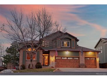 Inviting two-story home featuring a three-car garage, brick accents, and manicured lawn at dusk at 16873 Boreas Ct, Parker, CO 80134
