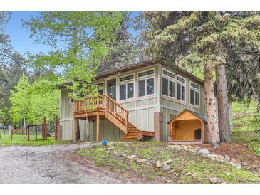 Charming home featuring a wooden porch and stairs, complemented by a matching dog house, set amongst mature trees at 30690 Highway 72, Golden, CO 80403