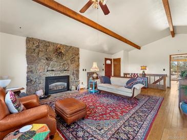 Cozy living room featuring a stone fireplace, exposed beams and hardwood floors at 24170 Matterhorn Dr, Indian Hills, CO 80454