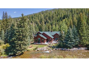 Beautiful exterior view of the red home surrounded by pine trees and flowing river at 189 Ginger Quill Ln, Breckenridge, CO 80424