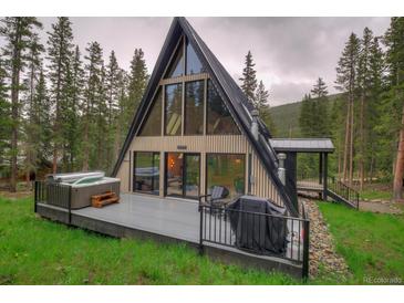 A-frame home featuring a modern design, large windows, a deck with a hot tub and grill, surrounded by lush trees at 563 Cr 672, Breckenridge, CO 80424