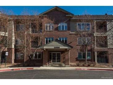 Brick apartment building with a covered entryway and visible unit numbers under a bright blue sky at 2896 W Riverwalk Cir # 204, Littleton, CO 80123