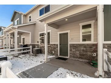 Charming townhouse featuring a covered entry, stone accents, and landscaped front yard with a partial white picket fence at 1353 Reynolds St # 16B, Fort Lupton, CO 80621