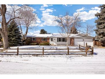 Charming single-story brick home with a two-car garage and a beautifully landscaped front yard covered in snow at 6803 Garland St, Arvada, CO 80004